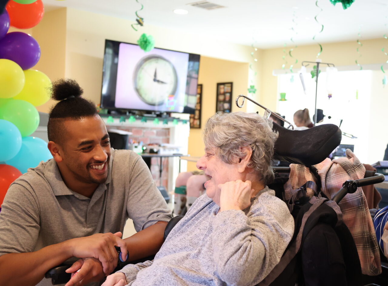 A staff member smiles and holds hands with a woman using a wheelchair during a community celebration.