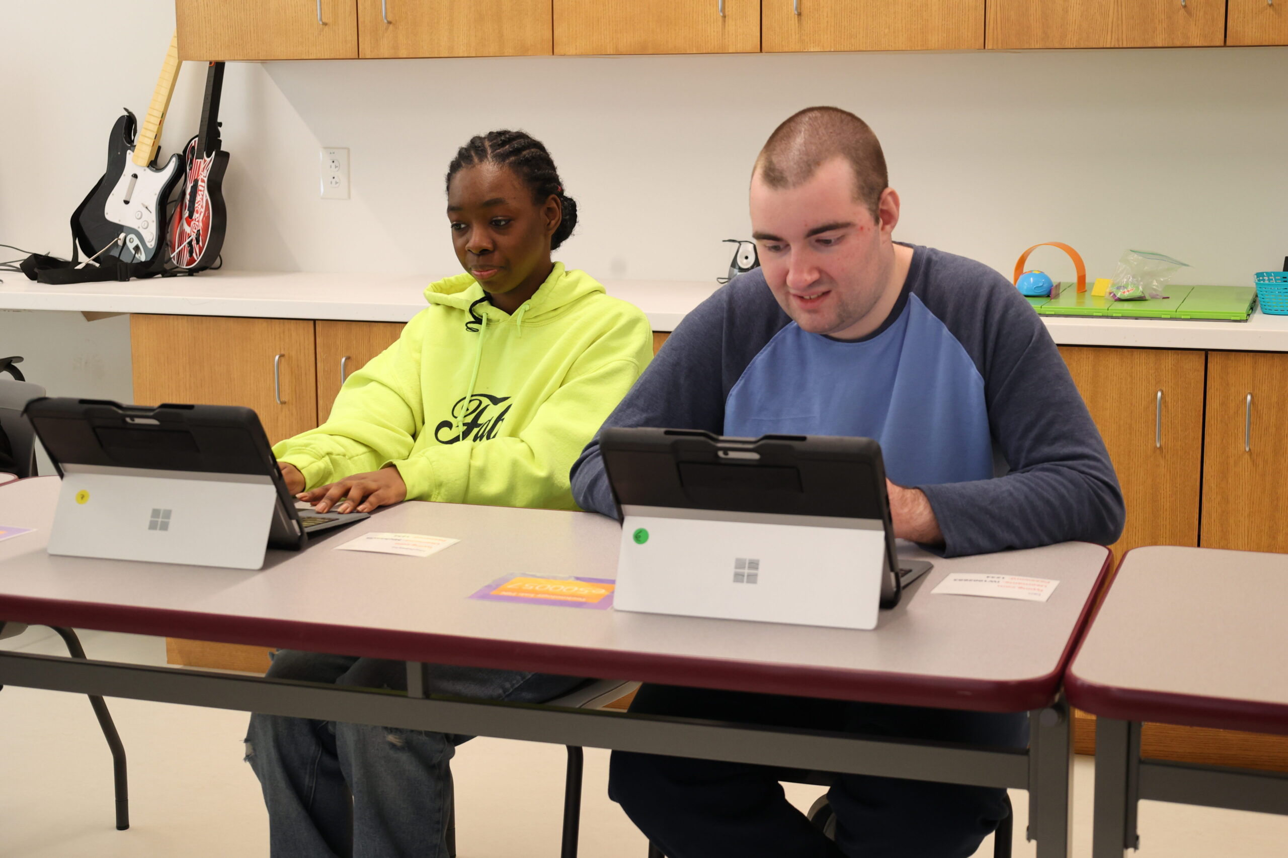 Two students seated at a classroom table using tablets during a learning activity.